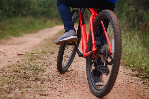 Toma de detalle de los pies de un joven en bicicleta por un camino forestal, practicando deportes en la naturaleza.