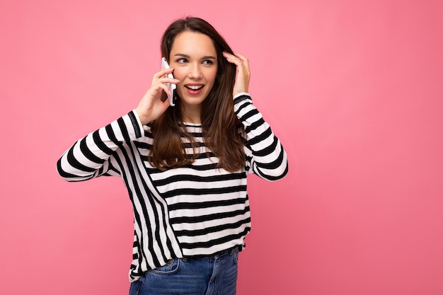 Foto toma de la foto de una atractiva joven emocional hablando en el teléfono inteligente con un suéter de rayas