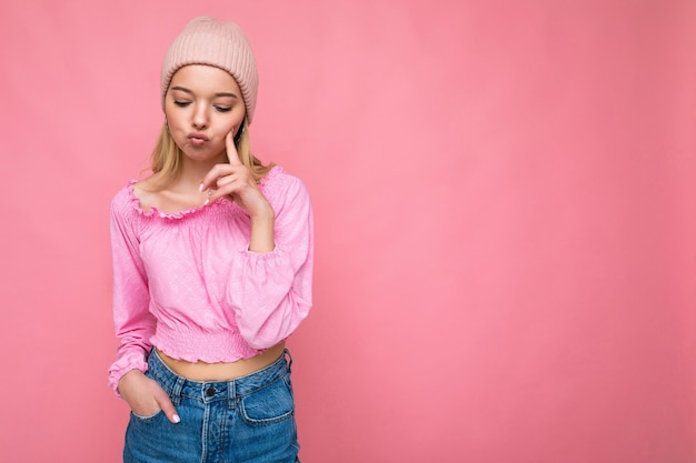 Toma de la foto de la hermosa joven rubia molesta triste aislada sobre fondo rosa vistiendo de pared