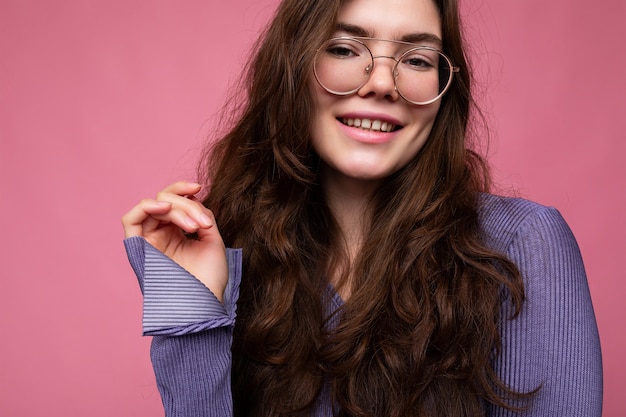 Toma de la foto de la hermosa mujer morena joven positiva con ropa casual y elegantes gafas ópticas aisladas sobre la pared de colores de fondo mirando a la cámara.