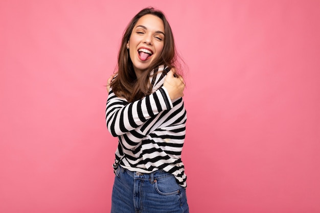 Toma de foto de lindo atractivo bastante joven divertido divertido mujer morena vistiendo casual manga larga a rayas aislado sobre fondo de colores con espacio de copia y mostrando la lengua