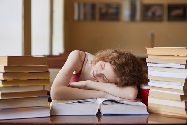 Toma interior de un estudiante cansado que duerme en el libro en la habitación roja, se cansó de estudiar, se durmió mientras leía material tutorial para las clases Concepto de educación, conocimiento y exámenes.