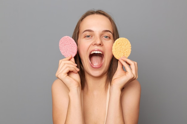 Toma interior de una mujer alegre y emocionada con esponjas cosméticas en las manos haciendo procedimientos cosméticos de buen humor y le gusta cuidar su piel perfecta