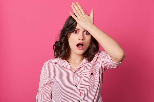 Toma interior de mujer joven olvidada frustrada mirando a la cámara con expresión facial preocupada, con la mano en la cabeza, la mujer se da cuenta de que se olvidó de hacer algo importante. Concepto de personas