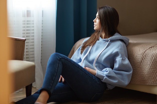 Toma interior de pensativa mujer de cabello oscuro vestida con sudadera azul