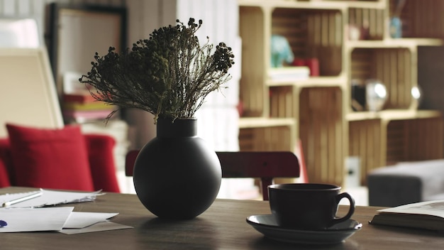 Toma de jarrón negro con flores secas y una taza en la mesa