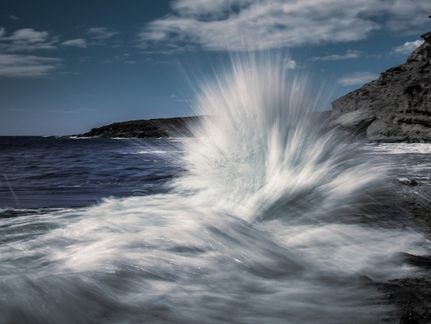 La toma de larga exposición de las olas rompiendo contra las rocas costeras parece una ráfaga de agua