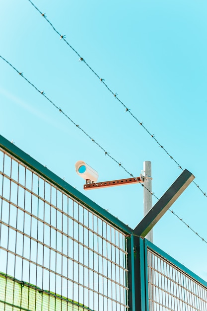 Una toma minimalista y colorida de una cámara de vigilancia con una pared y un alambre de púas.