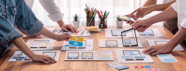 Toma panorámica del equipo de desarrolladores frontend intercambiando ideas sobre diseños de UI y UX para aplicaciones móviles en una interfaz de estructura metálica en papel Planificación del equipo de desarrollo de interfaces de usuario para un diseño de UI fácil de usar Examinar