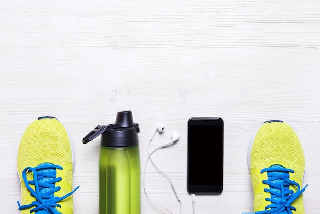 Foto toma plana de equipos deportivos zapatillas de deporte auriculares de agua y teléfono sobre fondo de madera