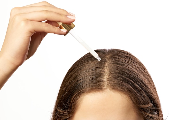 Una toma de primer plano de una persona aplicando un suero para el cabello o un tratamiento para el cuero cabelludo usando un gotero