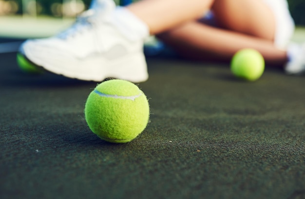 Toma una raqueta y una pelota y comienza a jugar Primer plano de una pelota de tenis en una cancha de tenis con una mujer irreconocible sentada en el fondo