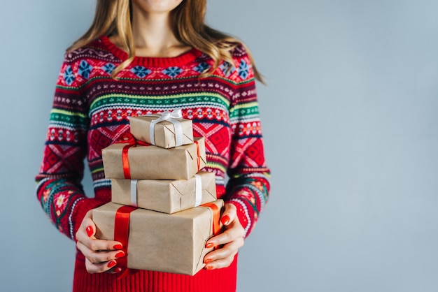 Toma recortada de chica rubia con uñas pulidas rojas sosteniendo un montón de cajas de regalo envueltas en papel artesanal