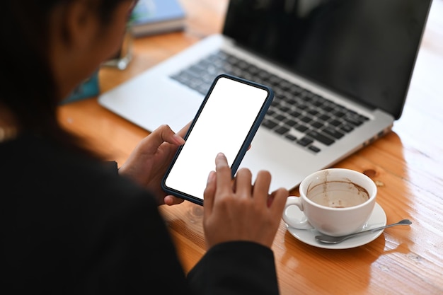 Toma recortada de empresaria usando smartphone recibiendo mensaje con confirmación haciendo transacción en computadora portátil.