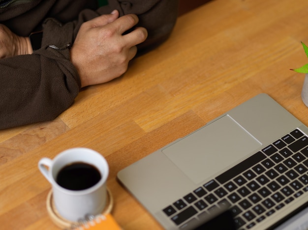 Toma recortada del hombre que trabaja con el portátil en la mesa de madera con taza de café