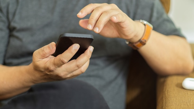 Toma recortada de hombre con smartphone mientras está relajado sentado en el sofá en la sala de estar