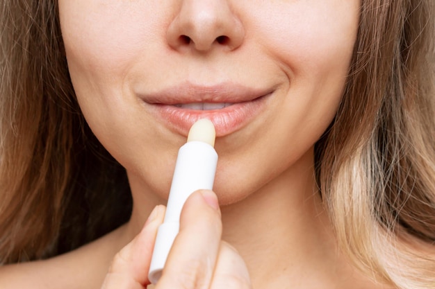 Toma recortada de una joven mujer rubia caucásica aplicando un lápiz labial higiénico blanco en sus labios
