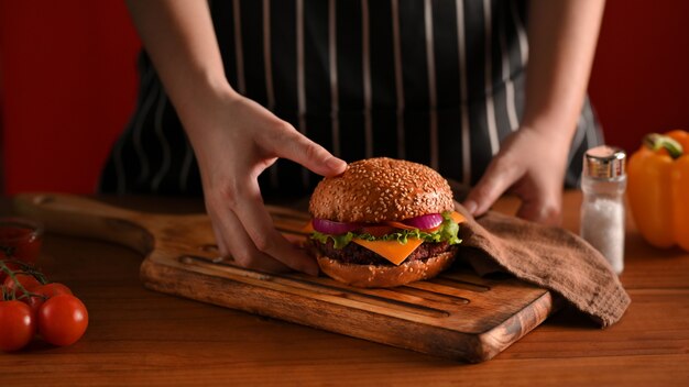 Toma recortada de la mano de la cocinera sosteniendo un delicioso lugar de hamburguesa de ternera a la parrilla en bandeja de madera para servir en el restaurante