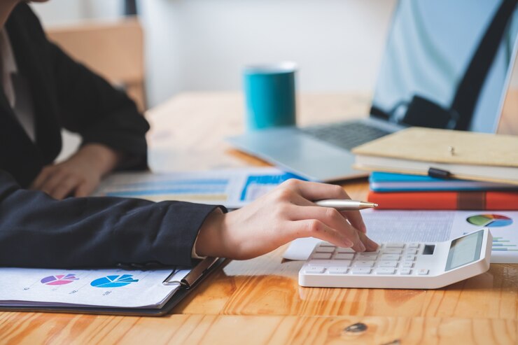 Toma recortada de la mano femenina en el trabajo casual de negocios en la calculadora mientras revisa el informe financiero