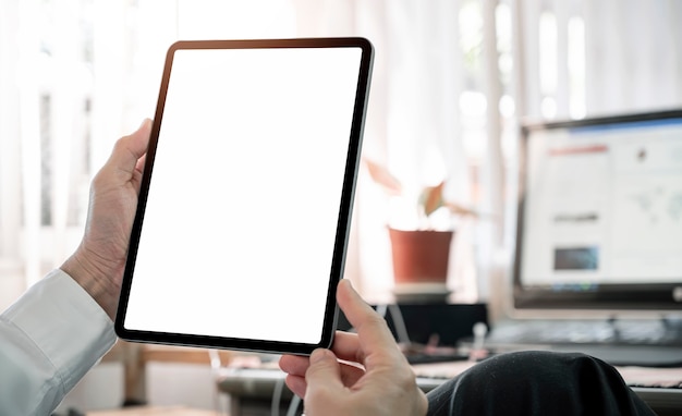 Toma recortada de la mano del hombre sosteniendo la tableta de pantalla en blanco mientras está sentado en el escritorio de la oficina