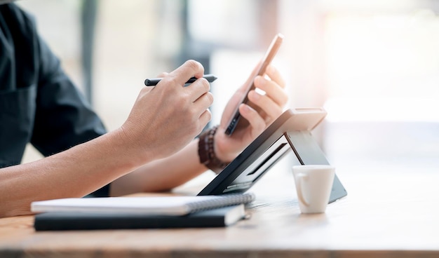 Toma recortada de la mano del hombre con teléfono inteligente y tableta portátil mientras está sentado en la mesa con espacio de copia, fotografía DOF superficial.