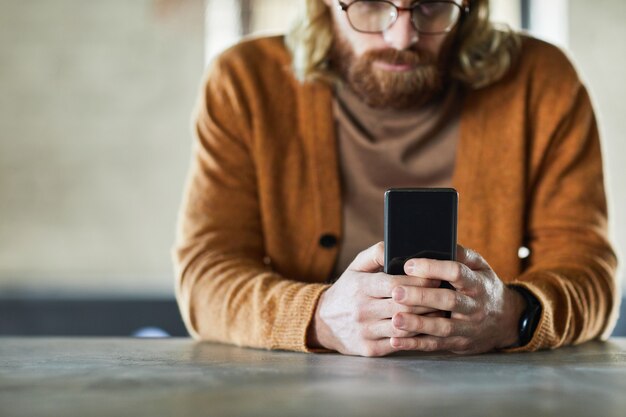 Toma recortada mínima de hombre barbudo mediante teléfono móvil con enfoque en manos masculinas sosteniendo el teléfono inteligente, espacio de copia