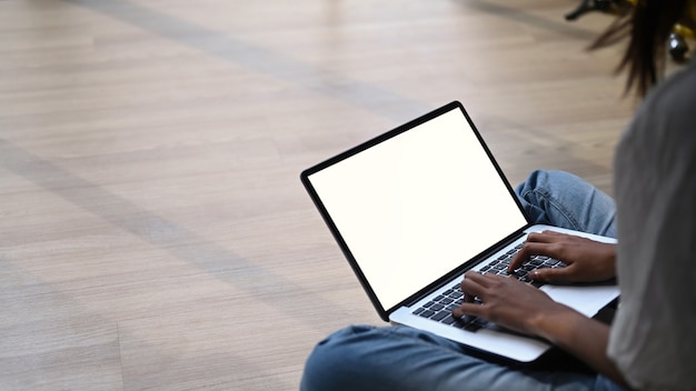 Toma recortada de mujer casual sentada en el piso en la sala de estar y trabajando en la computadora portátil.