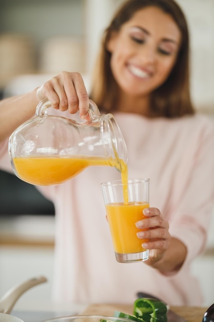 Foto toma recortada de una mujer joven bebiendo jugo de naranja fresco en su cocina.