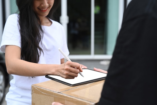 Toma recortada de mujer joven que firma en la recepción de la tableta digital del paquete de entrega del repartidor.