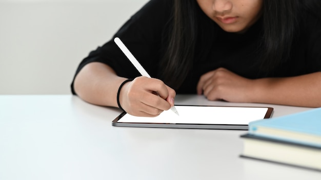 Toma recortada de niña haciendo sus deberes con tableta digital. Educación en línea e-learning.