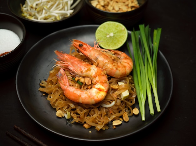 Toma recortada de Pad Thai, fideos tailandeses salteados con camarones en placa de cerámica negra con limón y cebollino