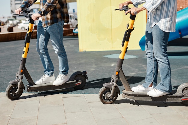 Toma recortada de pareja joven usando scooters eléctricos mientras viaja en las calles de la ciudad, espacio de copia