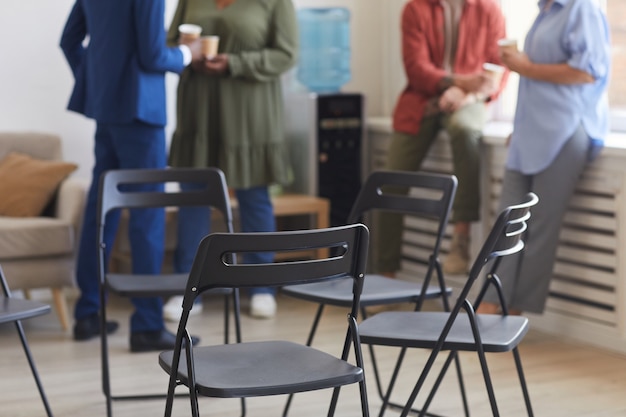 Toma recortada de sillas vacías en círculo durante la reunión del grupo de apoyo con gente charlando en la superficie, espacio de copia