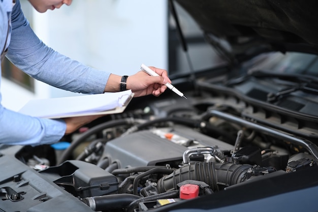 La toma recortada del técnico de automóviles asiático es el mantenimiento para los clientes de acuerdo con la lista de verificación de mantenimiento del vehículo especificada.