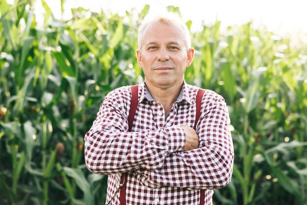 Foto toma de retrato de atractivo hombre caucásico de pie en el campo de maíz verde sonriendo alegremente a la cámara