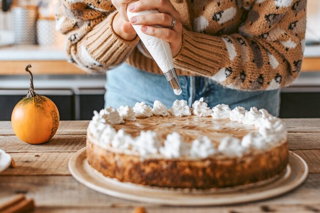 Toma selectiva de manos femeninas decorando un delicioso pastel de calabaza con crema