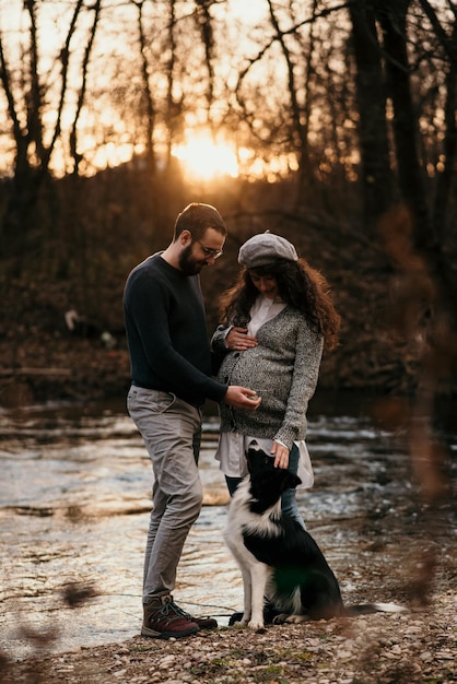 Una toma vertical de una pareja caucásica con su perro haciendo una sesión de fotos de maternidad en el parque.