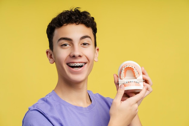 Tomada de cerca de una adolescente sonriente de cabello rizado con aparatos ortopédicos sosteniendo moldes dentales riendo