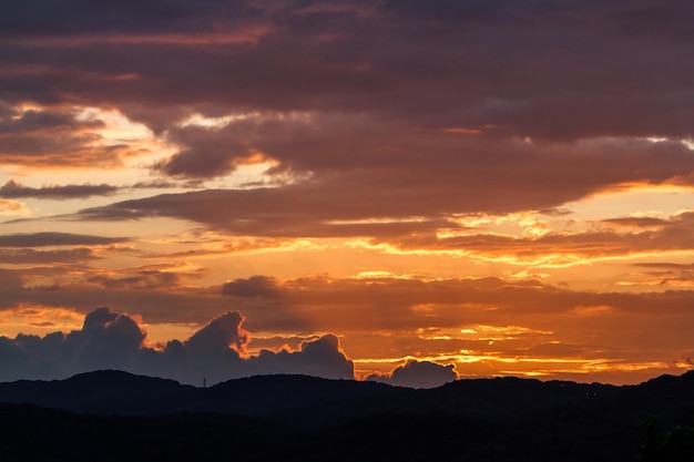 Tomada idílica de las montañas en silueta contra el cielo nublado naranja durante la puesta de sol