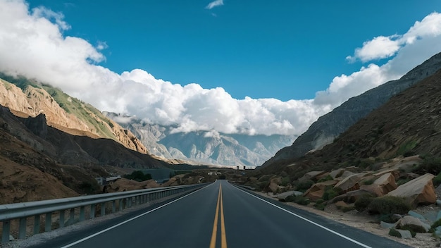 Tomada vertical de una carretera rodeada de altas montañas rocosas cubiertas de nubes blancas