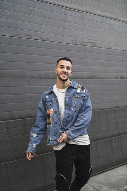 Tomada vertical de un joven hombre de moda en ropa de calle posando y sonriendo