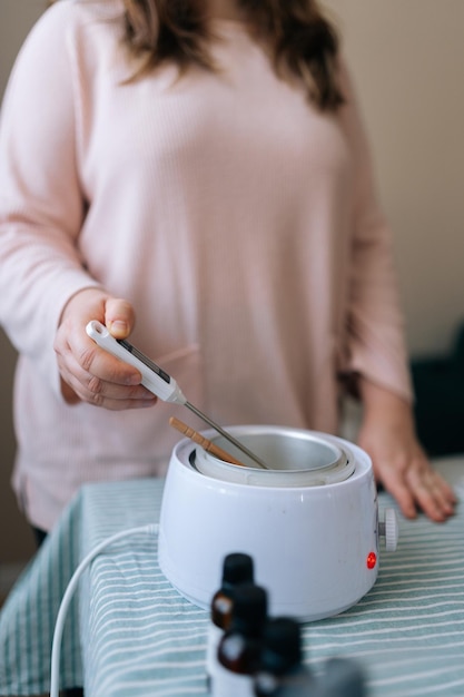 Tomada vertical recortada de una artesana mujer irreconocible midiendo la temperatura del proceso de cera derretida