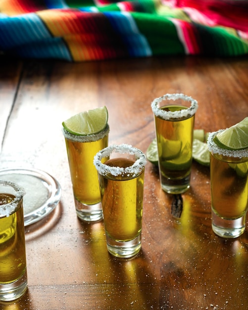 Foto tomadas de tequila con sal y limón en una mesa de madera fondo festivo
