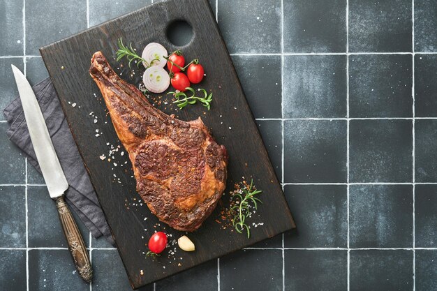 Tomahawk-Steak In Scheiben geschnittenes gegrilltes Tomahawk-Rindsteak mit gebackenen Kirschtomaten-Kräutern und Salz auf altem Holzhintergrund Vorbereitung zum Grillen Draufsicht und Kopierbereich