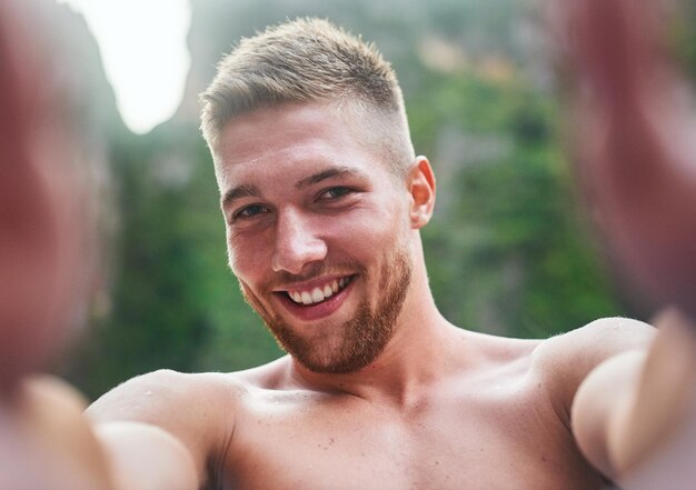 Tomando algunos recuerdos de las vacaciones Retrato de un joven apuesto que se toma una selfie afuera