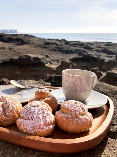 Foto tomando café negro por la mañana con canutillos sentado en la playa