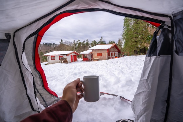 Tomando un café en una taza dentro de una tienda de campaña en una mañana de invierno camping libre de invierno