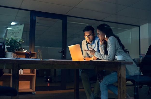 Tomando decisões importantes juntos para melhorar suas chances de sucesso Foto recortada de dois colegas trabalhando até tarde em um laptop em um escritório