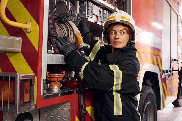 Tomando equipo del camión Mujer bombero en uniforme está trabajando en el departamento