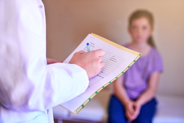 Tomando nota de cada sintoma Foto de um pediatra examinando uma garotinha em seu consultório